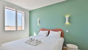 Ett modernt hotellrum med en stor säng, två vägglampor, ett fönster med utsikt och en liten vit pall.