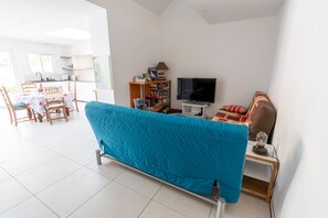 A modern living room with a sofa, a TV, a bookshelf, and a dining area with chairs and a table. - Maison Pépin - avec joli jardin (Les Sables d'Olonne)