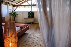 Een slaapkamer met houten vloer, een bed, een bad en een hangende plant.