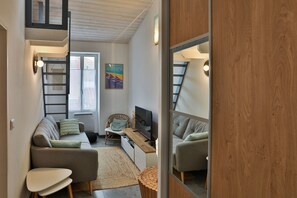 Un espace de vie compact comprenant une chambre en mezzanine, un canapé, un téléviseur et un plancher en bois.