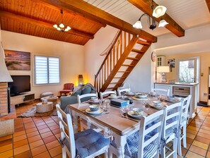 A dining area with a wooden table set for four, a TV, and a staircase leading to an upper level. - Petit Havre de paix - Three Bedroom House, Sleeps 7 (Longeville-sur-Mer)