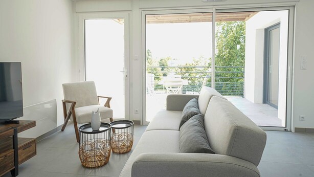 A modern living room with a sofa, a chair, a TV, and a balcony with a table and chairs.