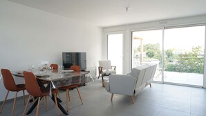 A modern living room with a dining table, chairs, a sofa, and a TV.