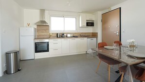 A modern kitchen with white cabinetry, a stainless steel refrigerator, an oven, a microwave, and a dining area with a table set for two.