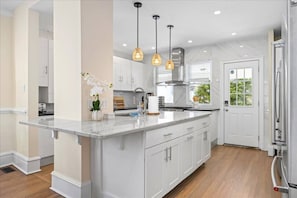 A modern kitchen with a marble island, pendant lighting, and a view of the outdoors. - Luxury Beach Block | Sauna + Cold Plunge + Hot Tub (Ventnor City)