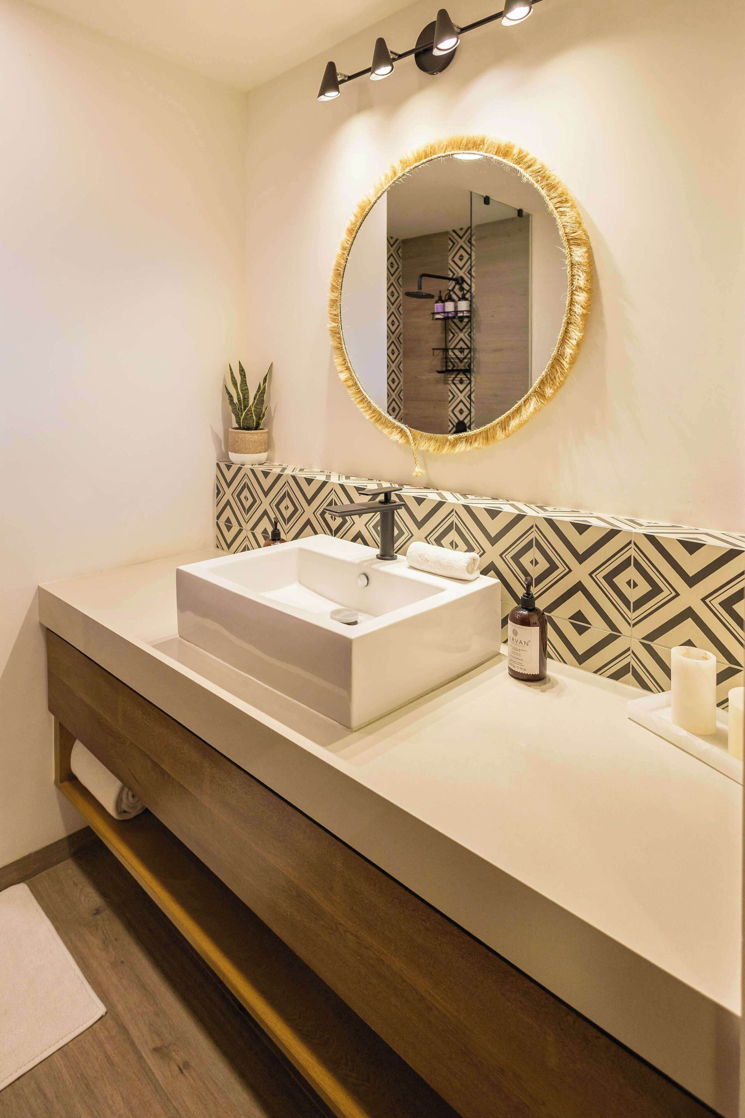 A modern bathroom with a rectangular sink, a round mirror with a golden frame, and patterned wall tiles.
