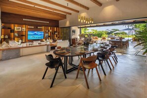 A modern dining area with a large round table, black and wooden chairs, and a television on the wall. - Ultra-Luxe 5BR Retreat • Private Pool • Golf Cart (Corral del Risco)