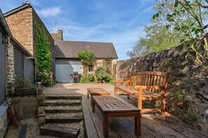 A stone building with a wooden bench and table, a gravel path, and a garage door. - Ty Rance - Maison Avec Terrasse (Plouër-sur-Rance)