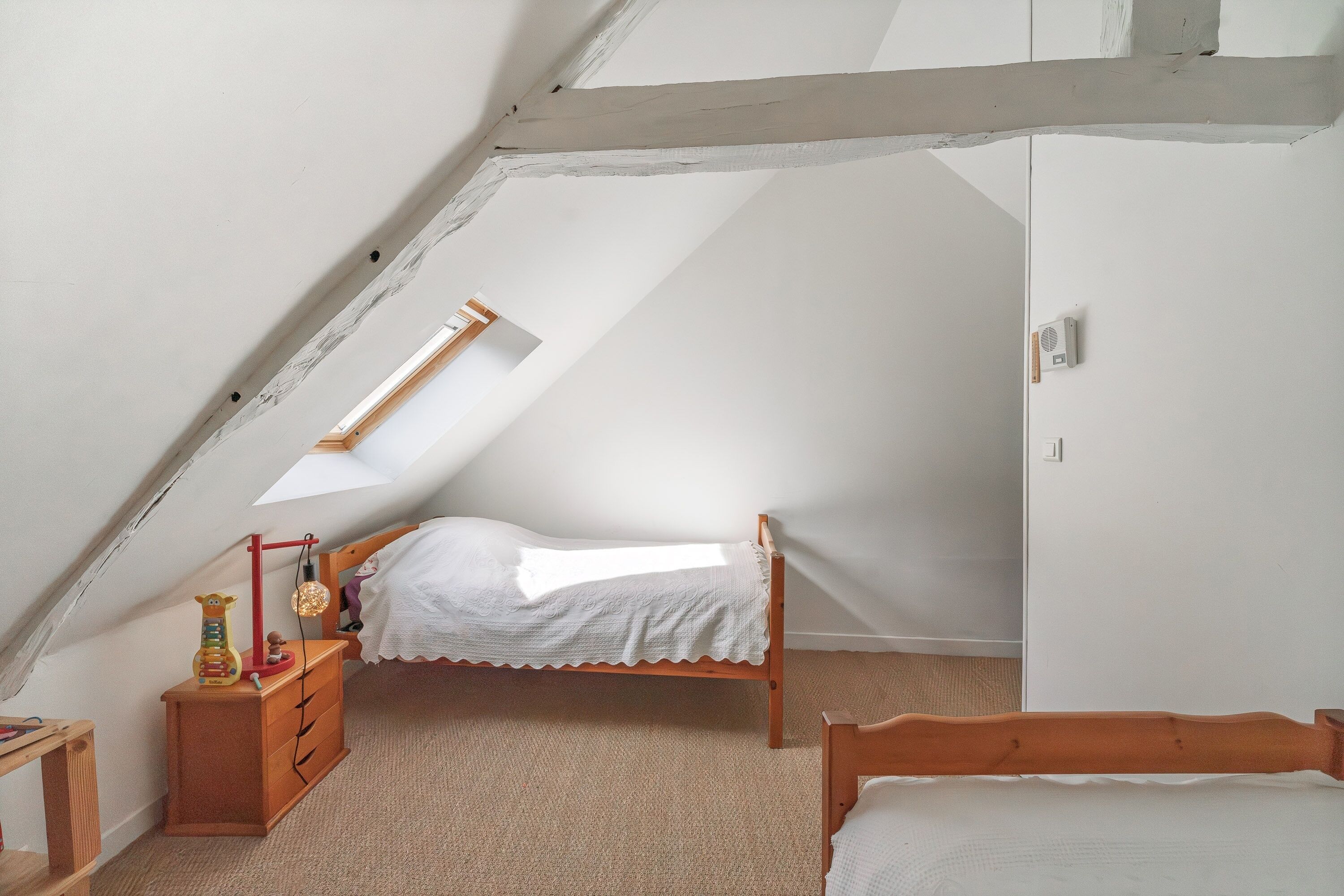 A bedroom with a sloped ceiling, a bed, a dresser, and a small table with toys.