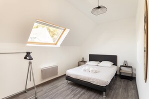 Ein Schlafzimmer mit Oberlicht, einem Bett, einem Nachttisch, einer Lampe und einem Stativ.