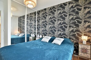 Ein Schlafzimmer mit einer Spiegelwand, einem Bett mit blauer Bettwäsche und einem Nachttisch mit einer Lampe.