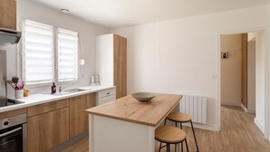 Et moderne køkken med træskabe, en central ø, barstole og udsigt til et tilstødende rum.