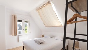Et soveværelse med seng, et vindue med gardiner, en radiator og et lille bord med en fugleburet.