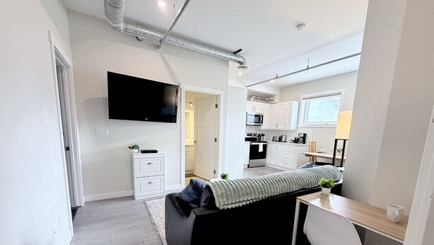 Un apartamento moderno con kitchenette, televisión de pantalla plana, sofá, escritorio y una silla.