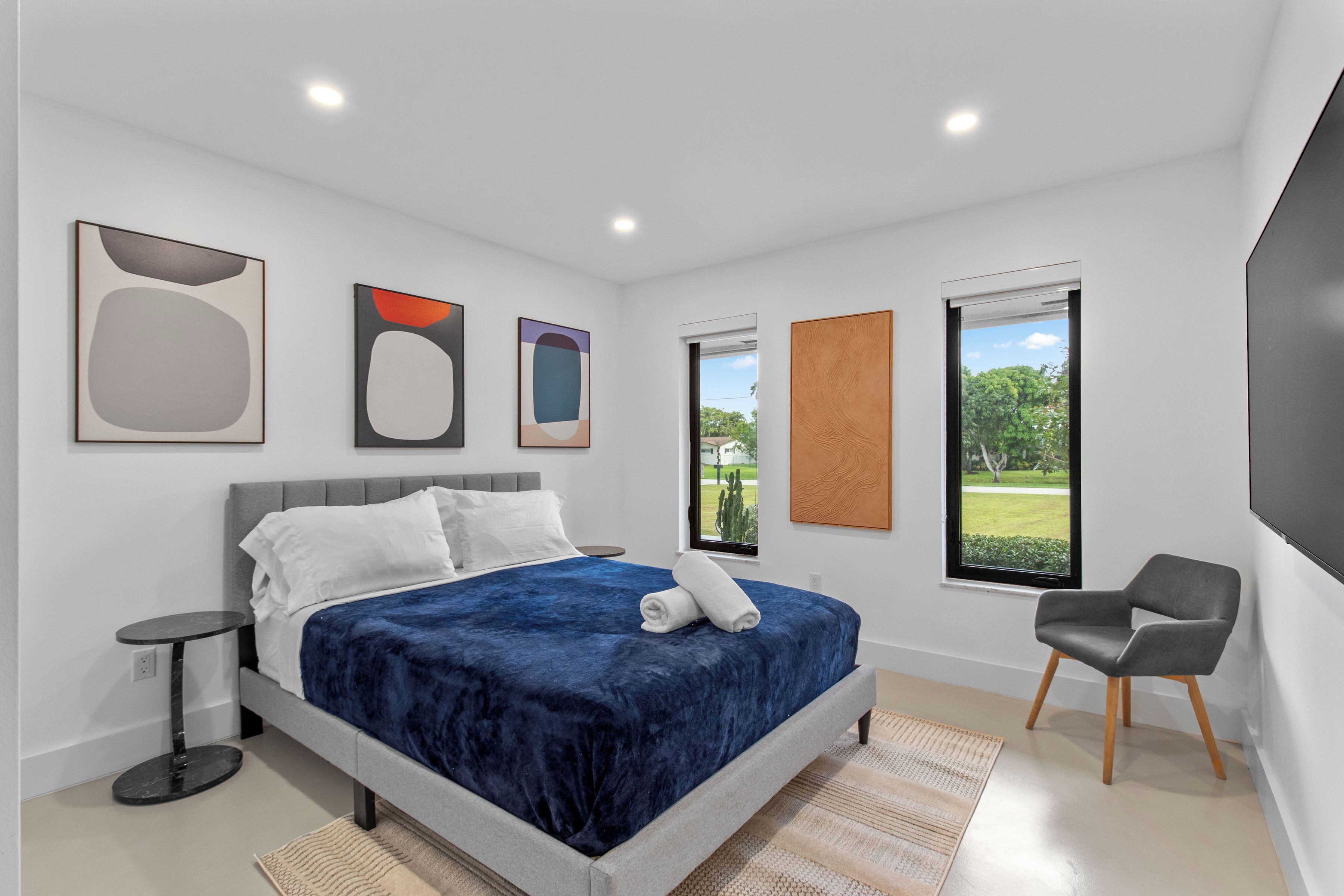 A modern bedroom with a bed, a chair, and artwork on the walls.