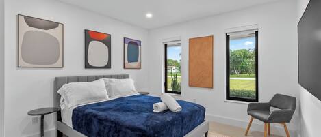 A modern bedroom with a bed, a chair, and artwork on the walls.