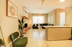 Uma sala de estar moderna com sofá, espaço para refeições, uma cadeira verde, planta em vaso e um relógio na parede.