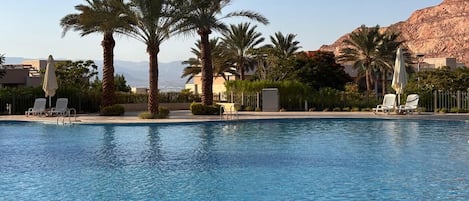 A swimming pool with palm trees, lounge chairs, and a mountainous backdrop.