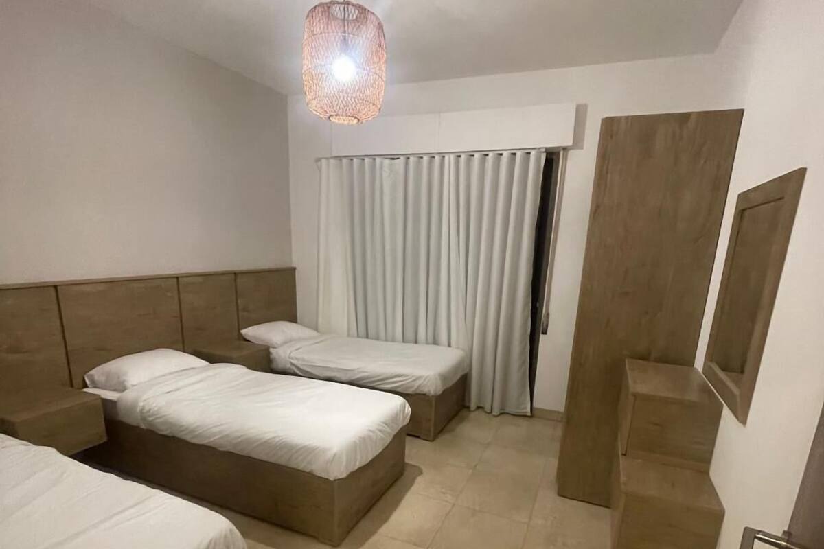 Ein Hotelzimmer mit zwei Betten, einer Deckenleuchte, einem Fenster mit Vorhängen und einer Tür.