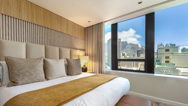 A hotel room with a large bed, a view of the city, and a wooden headboard. - Foreshore Luxury Place (Cape Town City Centre)