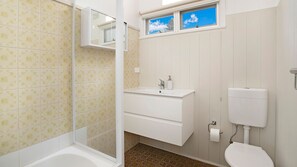 Et badeværelse med badekar, vask, toilet og et vindue med udsigt til himlen.