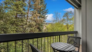 Un balcon avec une table et des chaises, donnant sur une zone boisée et sur un bâtiment situé au loin.