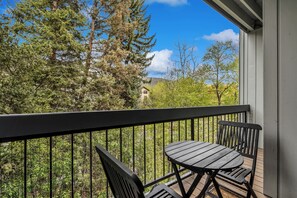Ein Balkon mit Tisch und Stühlen mit Blick auf eine bewaldete Gegend und ein Gebäude in der Ferne.