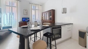 Cozinha moderna com ilha central, sala de jantar com sofá e televisão ao fundo.