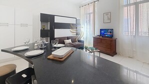 Cozinha moderna com área de refeições, sofá e televisão.