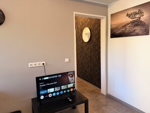 Uma televisão exibindo a interface Google TV com diversos aplicativos, um espelho fixado na parede e um quadro com uma paisagem.