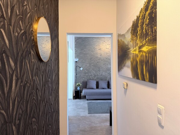 Ein modernes Interieur mit strukturierter Wand, rundem Spiegel, grauem Sofa und einem Waldgemälde.