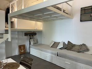 A bunk bed with a desk and storage, a small seating area with cushions, a wooden anchor decoration, and a wall-mounted shelf. - Le Petit | Luxury Loft in the Heart of Sperlonga - Easy Access (Sperlonga)