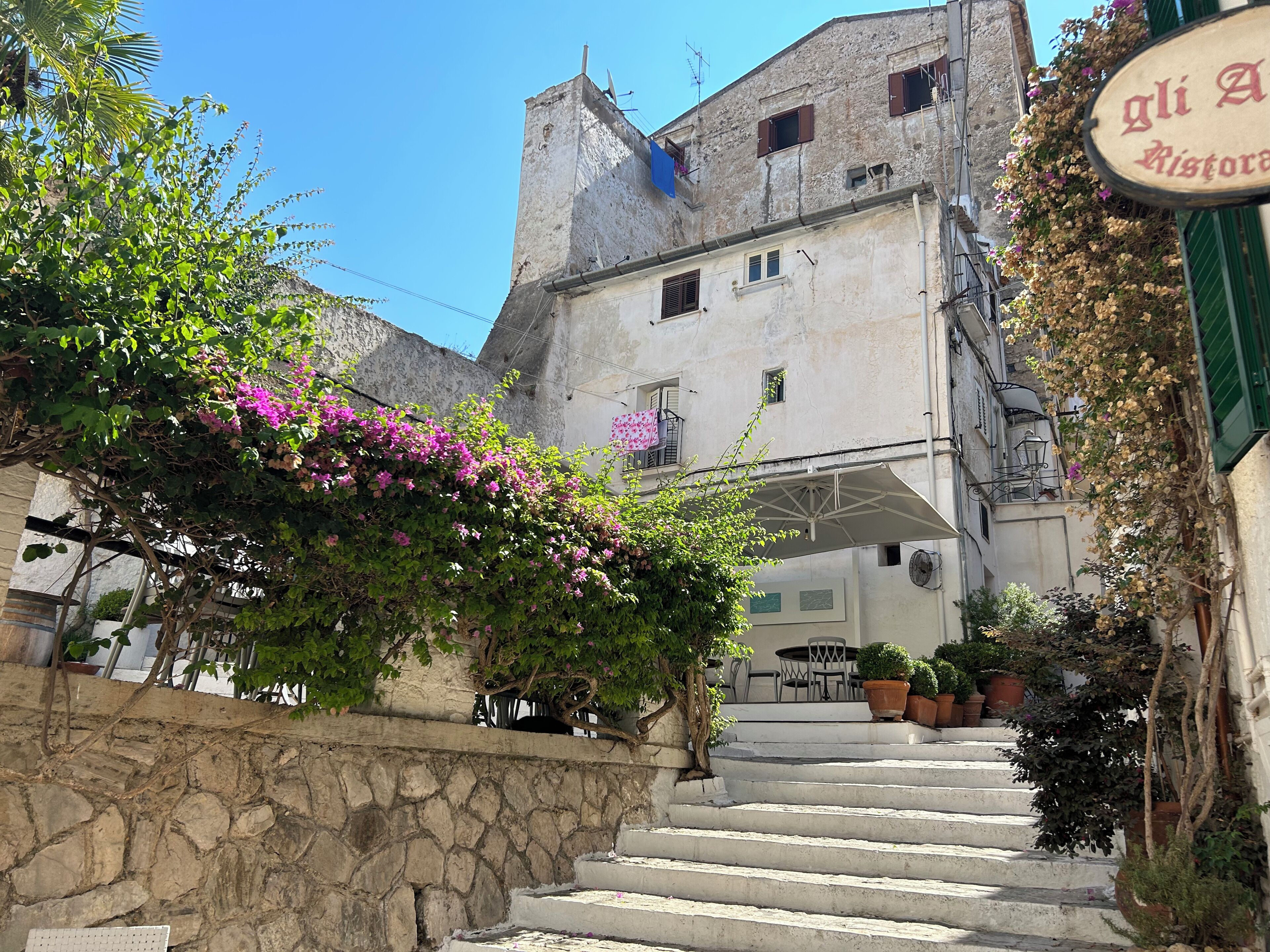 A building with a stone staircase leading to a terrace with outdoor furniture.