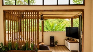 A room with a wooden dining table, chairs, a TV, a speaker, and a balcony with plants. - Casa Toucan - Jungle Pool Villa - Private Pool -  Starlink - Quads (Isla Colon)