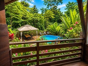 En træterrasse med swimmingpool, omgivet af frodig vegetation og en pavillon.