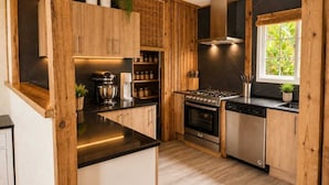 A modern kitchen with wooden cabinets, a gas stove, a dishwasher, and a window with a view of greenery. - Casa Toucan - Jungle Pool Villa - Private Pool -  Starlink - Quads (Isla Colon)