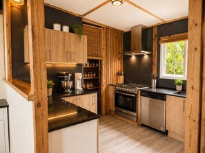 Une cuisine moderne avec des meubles en bois, une cuisinière à gaz, un lave-vaisselle et une fenêtre donnant sur un paysage verdoyant.