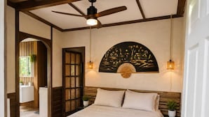 A bedroom with a bed, wooden headboard, ceiling fan, wall art, and two bedside lamps. - Casa Toucan - Jungle Pool Villa - Private Pool -  Starlink - Quads (Isla Colon)