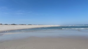 Ein Strand mit weitem, sandigen Ufer, ruhigem Wasser und blauem Himmel.