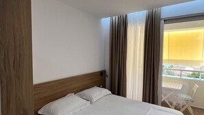 Camera d'albergo con un letto con struttura in legno, biancheria bianca e un balcone con tavolo e sedie.