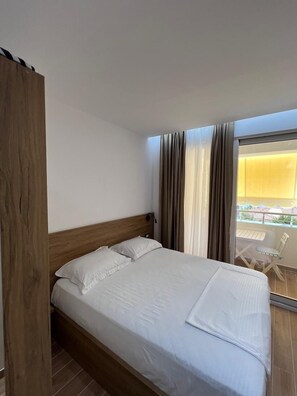 Ein Hotelzimmer mit einem Bettgestell aus Holz, weißer Bettwäsche und einem Balkon mit Tisch und Stühlen.