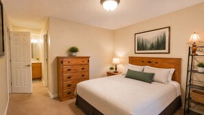 Une chambre à coucher comprenant un lit, une commode, une table de chevet, une lampe, un tableau encadré et une étagère avec des plantes.