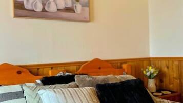 A bedroom with a bed, pillows, a headboard, a painting, and a nightstand with a vase.