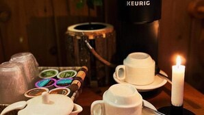 Una cafetera, tazas, un hervidor y una vela sobre una mesa de madera.