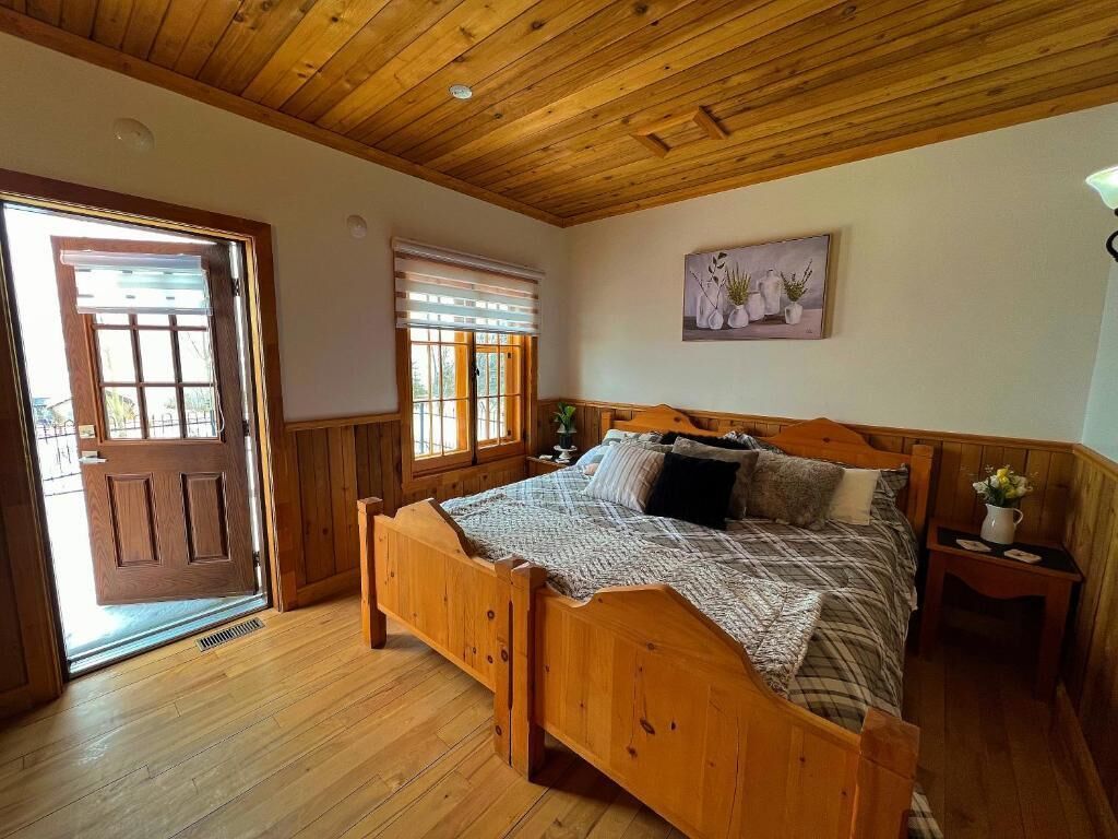 Una cama con estructura de madera en una habitación con techo de madera, una puerta y una ventana con persianas.