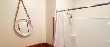 Een badkamer met toilet, bad, douchegordijn en spiegel.