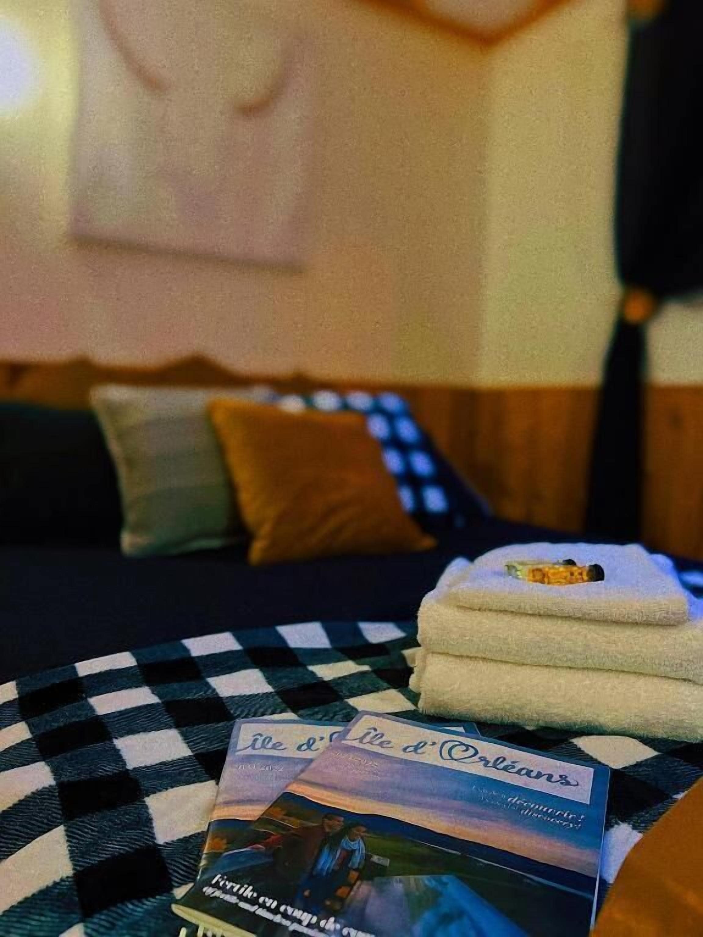 Una cama con una manta a cuadros, una pila de toallas blancas y un folleto titulado 'Île d'Orléans'.