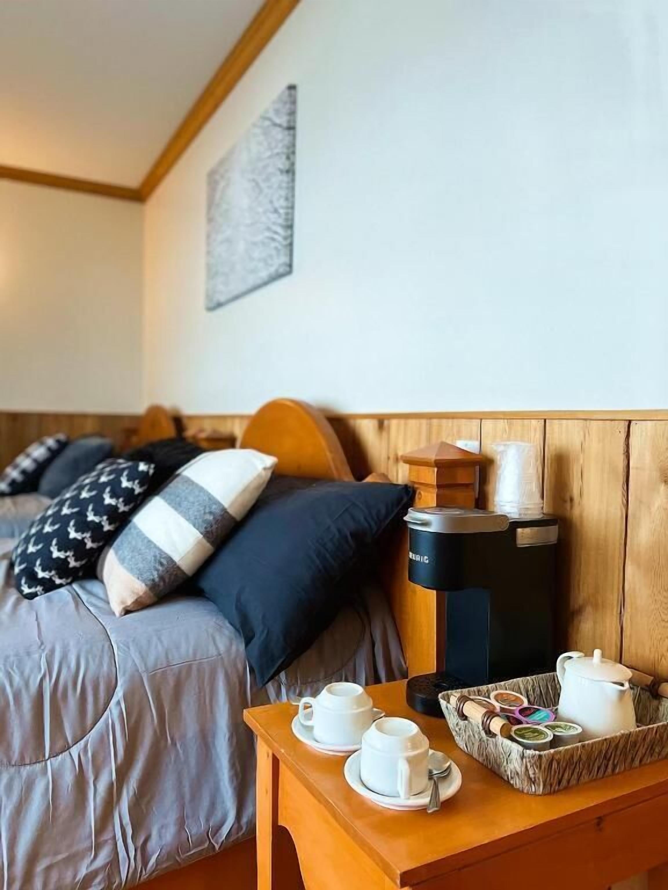 Una habitación de hotel con cama, almohadas, cafetera y una bandeja con tazas y tetera.