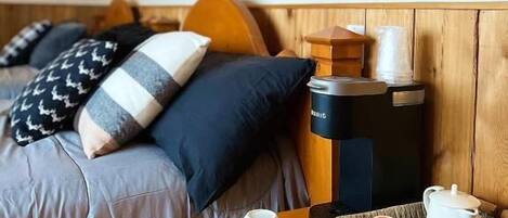 Una habitación de hotel con cama, almohadas, cafetera y una bandeja con tazas y tetera.