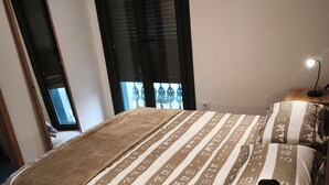 Ein Schlafzimmer mit einem Bett, einem Nachttisch, einer Lampe und einem Fenster mit Jalousien.